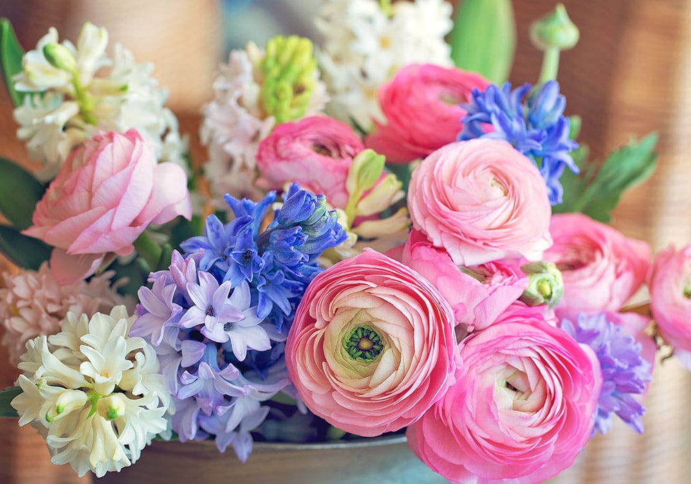 A bouquet of various flowers with a mix of pink ranunculus, white and blue hyacinths in a soft-focus indoor setting.